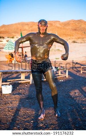 DEAD SEA RESORT, JORDAN - APR 30, 2014: Unidentified man in Dead Sea mud poses for the camera. The mud of Dead Sea is being used with  the therapy purposses for the people with skin problems
