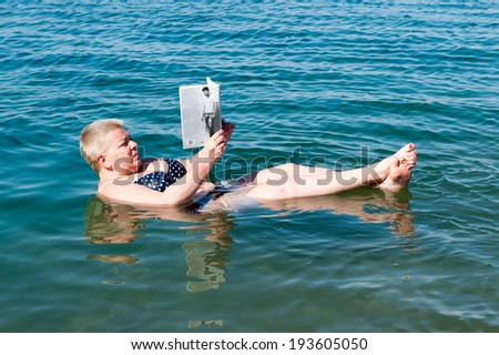 DEAD SEA RESORT, JORDAN - MAY 1, 2014: Unidentified woman reads a book laying on the water surface of the Dead Sea. Dead Sea water is used for medical purposes for the people with skin problems