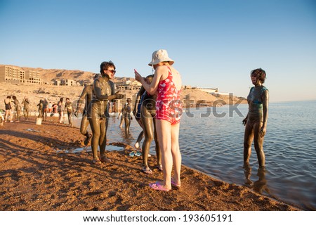 DEAD SEA RESORT, JORDAN - APR 30, 2014: Unidentified Chinese tourists in the mud of the Dead Sea. Dead Sea mud posesses the medical qualities and helps to the people with skin problems