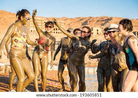 DEAD SEA RESORT, JORDAN - APR 30, 2014: Unidentified Chinese tourists pose in the mud of the Dead Sea. Dead Sea mud posesses the medical qualities and helps to the people with skin problems