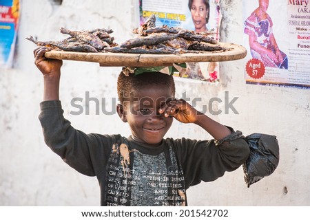 ACCRA, GHANA - MARCH 3, 2012: Unidentified Ghanaian smiling little boy offers to buy a fish in Ghana. People of Ghana suffer of poverty due to the unstable economic situation