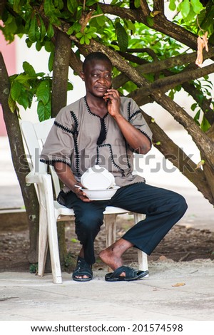 ACCRA, GHANA - MARCH 4, 2012: Unidentified Ghanaian man eats and speaks on a phone in the street in Ghana. People of Ghana suffer of poverty due to the unstable economic situation