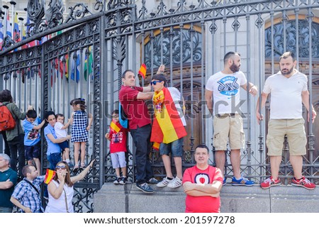 MADRID, SPAIN - JUN 19, 2014: Unidentified Spanish people with national flags on a fence in  centre of Madrid on a case the celebration on a day of the inauguration of the New King of Spain Felipe IV