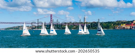 LISBON, PORTUGAL - JUN 20, 2014:  Yachts sailing near the Bridge 25 of April in Lisbon, Portugal. It was inaugurated on August 6, 1966