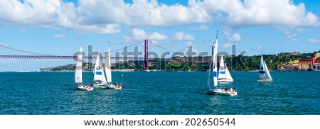 LISBON, PORTUGAL - JUN 20, 2014:  Yachts sailing near the Bridge 25 of April in Lisbon, Portugal. It was inaugurated on August 6, 1966