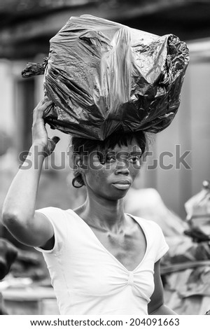 ACCARA, GHANA - MAR 4, 2012: Unidentified Ghanaian woman walks with a bag of garbage on her head in black and white. People of Ghana suffer of poverty due to the unstable economical situation