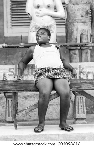 ACCARA, GHANA - MAR 2, 2012: Unidentified Ghanaian fat woman sits on a bench in black and white. People of Ghana suffer of poverty due to the unstable economical situation