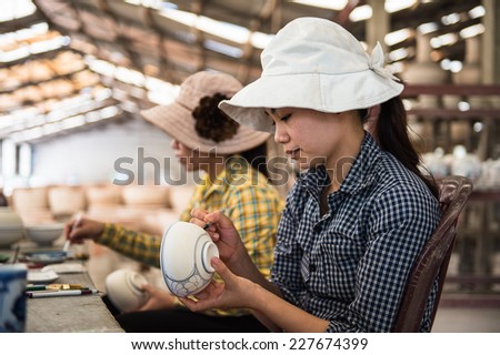 HANOI, VIETNAM - SEP 24, 2014: Unidentified Vietnamese woman draws on the ceramic dish in the ceramic workshop. Ceramic art is very popular in Asian culture