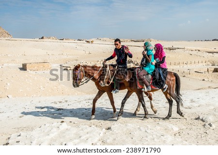 GIZA, EGYPT - NOV 23, 2014: Unidentified Egyptian man and two tourists ride horses in  Giza Necropolis, Egypt. UNESCO World Heritage