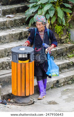 SAPA, VIETNAM - SEP 22, 2014: Unidentified Hmong woman in traditional clothes checks the garbage in the street in Sapa. Hmong is on of the minority eethnic group in Vietnam