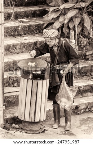SAPA, VIETNAM - SEP 22, 2014: Unidentified Hmong woman in traditional clothes checks the garbage in the street in Sapa. Hmong is on of the minority eethnic group in Vietnam