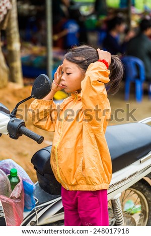 TA PHIN, LAO CAI, VIETNAM - SEP 21, 2014:  Unidentified Red Dao girl in orange jacket checks her look in a motocycle mirror. Red Dao is one of the minority ethnic groups in Vietnam