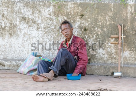 LUANG PRABANG, LAOS - SEP 25, 2014: Unidentified Lao poor man sits in the street. 55% of Laos people belong to the Lao ethnic group