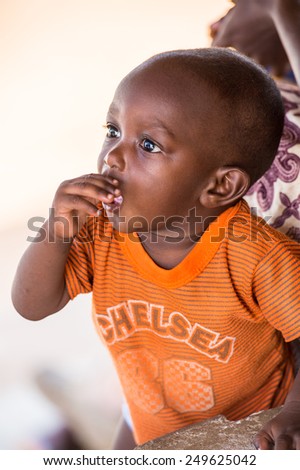 KARA, TOGO - MAR 9, 2013: Unidentified Togolese little baby boy in an orange shirt close up. People in Togo suffer of poverty due to the unstable econimic situation