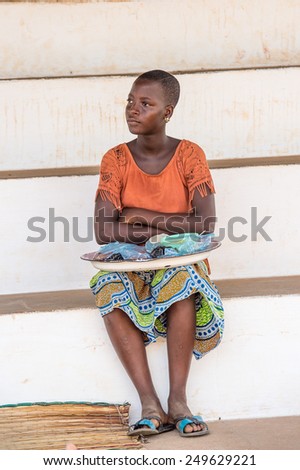 KARA, TOGO - MAR 9, 2013: Unidentified Togolese woman in an orange shirt with a tray. People in Togo suffer of poverty due to the unstable econimic situation