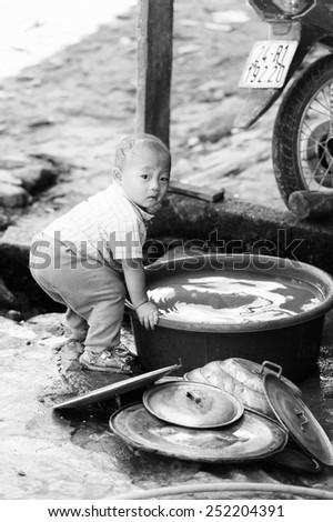 LAO CHAI VILLAGE, VIETNAM - SEP 22, 2014: Unidentified Hmong little boy helps his mother to wash the dishes in Lao Chai. Hmong is on of the minority eethnic group in Vietnam