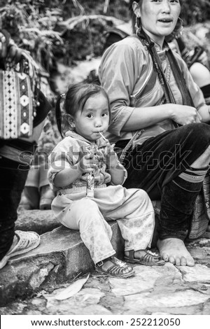 CATCAT, VIETMAN - SEP 20, 2014: Unidentified Hmong cute girl eats a candy in CatCat village, Vietnam. Hmong is a minority ethnic group of Vietnam