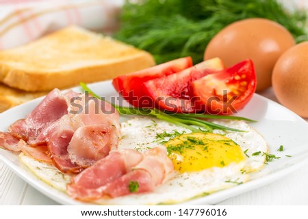 Fried eggs with ham and tomatoes on a white plate