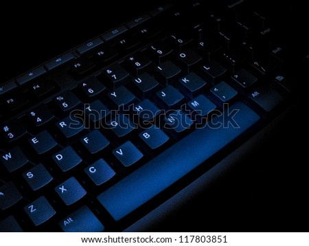 Rough surface of keyboard covered in a bunch of blue light. Low-key image. Few parts look like noise that actually are its rough surface.