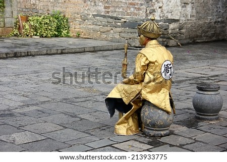DA LI, CHINA - AUGUST 24: A performer acts as an ancient Chinese soldier sitting beside road of entrance to ancient Da Li town welcoming tourists on August 24 in Dali, China.