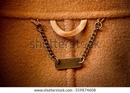 Close-up of metal hanging chain with blank tag inside brown woolen coat.
