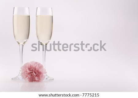 Two glass champagne flutes with a carnation against a plain background.