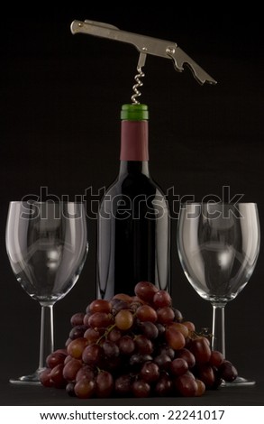 A Bottle of red wine with glasses,corkscrew and grapes on a plain background
