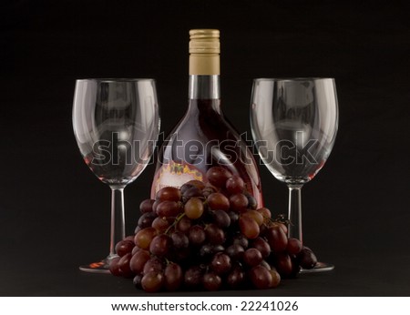A Bottle of rose wine with grapes and wine glasses on a plain background