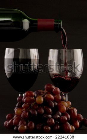 Two glasses of red wine being poured with grapes on a plain background