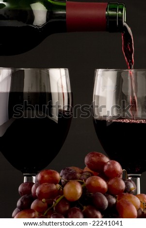 Two glasses of red wine being poured with grapes on a plain background