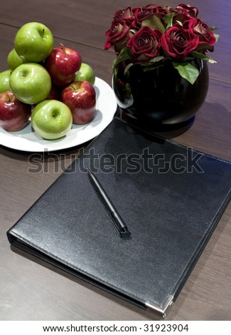 A blank corporate display book with a bowl of apples and red roses.