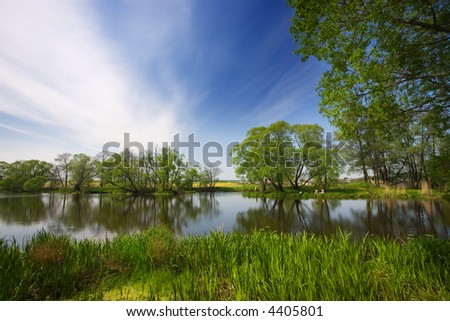 The lake, the trees reflected in water, the sky with plumose clouds, are visible small figures of having a rest people