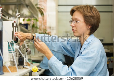The young nice woman-scientist work with syringe on a background scientific instruments