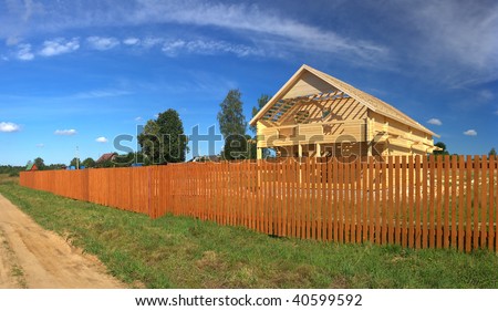 A new home being built with wood behind a brown fence (Panorama)
