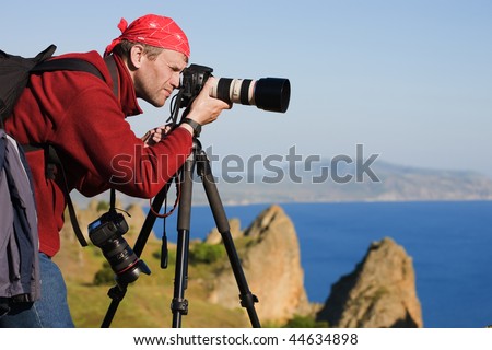 The photographer with the camera on a tripod. On a background the sea and rocks
