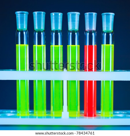 Five test tubes with a green fluorescing liquid and one with a red liquid in a support on a dark blue background.