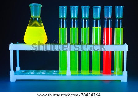 Five test tubes with a green fluorescing liquid and one with a red liquid in a support and yellow flask on a dark blue background.