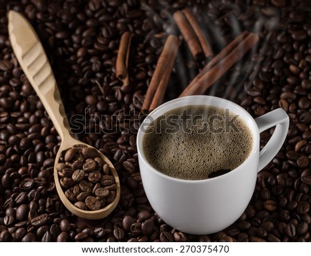 Cup of freshly brewed French coffee with cinnamon sticks and a wooden spoon on a background of beans