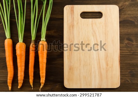 Bunch of fresh carrots with green leaves and cutting board on wooden background. Healthy vegetarian food