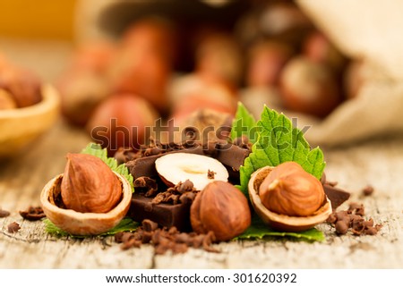 hazelnut with chocolate bars and green leaves on old wooden background