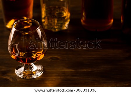 glass of whiskey with ice and a bottle on a wooden table. Cognac, brandy.