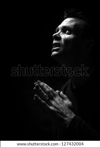 A black and white image of a man kneeling down praying to God.