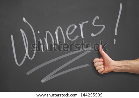 Mans hand with a thumbs up in front of a winners message on a chalkboard.