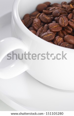 White mug with coffee beans in it on a white isolated background.