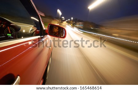 A man driving a car at night showing the wheel, mirror and dashboard.