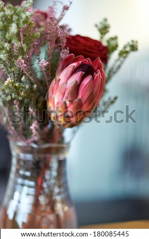 Narrow focus flowers in a glass jug on a wooden table.