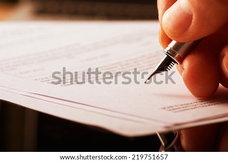A hand holding a fountain pen and about to sign a letter. Styling and small amount of grain applied.