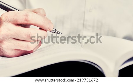 A hand holding a fountain pen and about to writer a note or highlight some text for correction. Styling and small amount of grain applied.