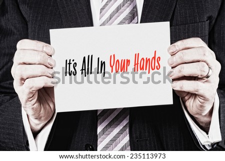 A businessman holding a business card with the words, It\'s All In Your Hands, written on it.