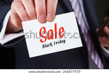 A businessman holding a business card with the words, Sale - Black Friday, written on it.